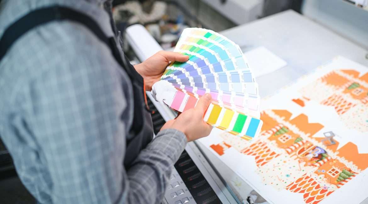 Print house worker controlling printing process quality and checking colors with magnifying glass.