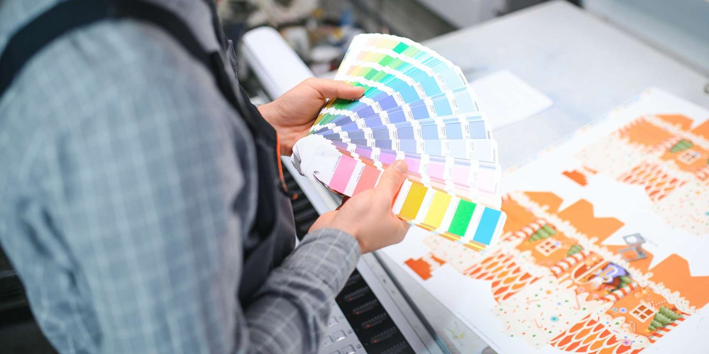 Print house worker controlling printing process quality and checking colors with magnifying glass.